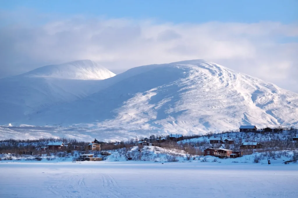Beautiful scenery of buildings at foot of snowy mountains on coast of Lake Torneträsk (Tornestrask) around Abisko National Park (Abisko nationalpark). Sweden, Arctic Circle, Swedish Lapland